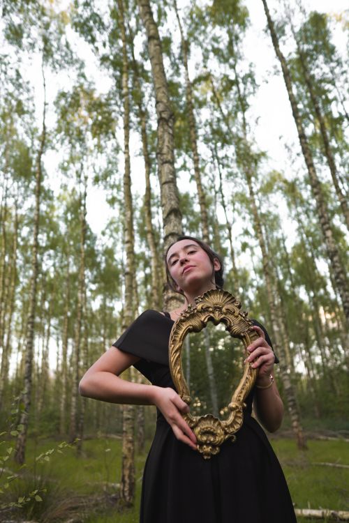 Free Artistic shot of woman in black dress holding a vintage mirror in a lush forest. Stock Photo