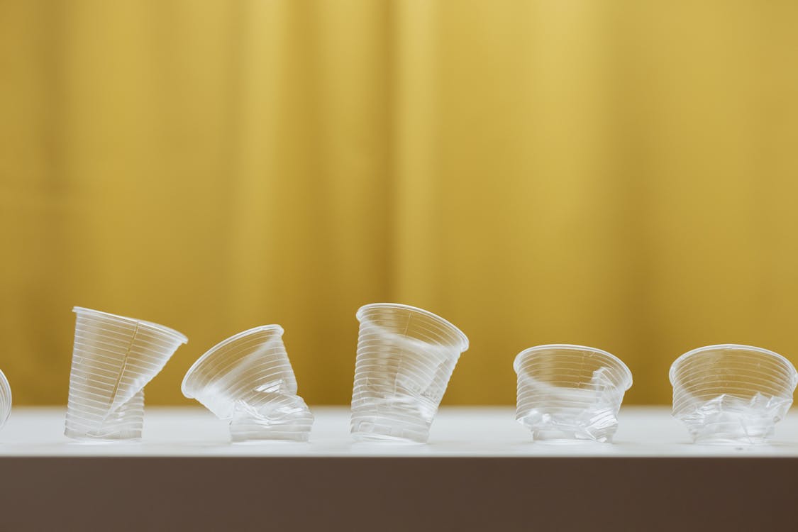Free Minimalist image showing crumpled plastic cups against a yellow background on a table. Stock Photo