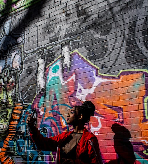 Woman in Red Jacket Standing Near Brick Wall Holding a Cellphone 