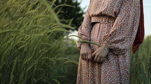 Free Unrecognizable crop female in boho dress standing in green meadow among tall grass in countryside Stock Photo