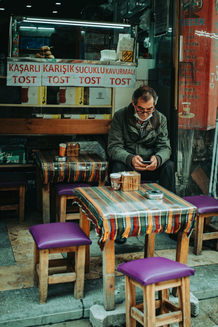 A Man In Black Jacket Sitting On A Chair Outside