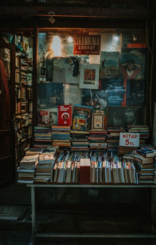 Free Charming bookstore window showcasing stacks of vintage books and retro posters, perfect for book lovers. Stock Photo