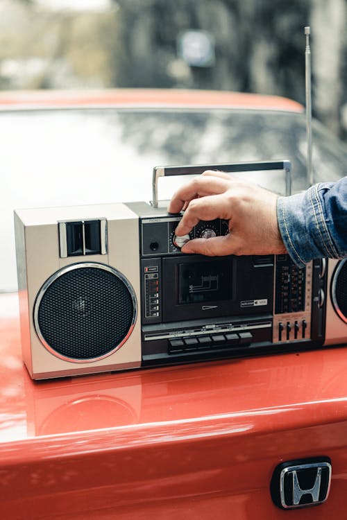 Free Crop anonymous male turning switch on portable boombox placed on red car trunk Stock Photo