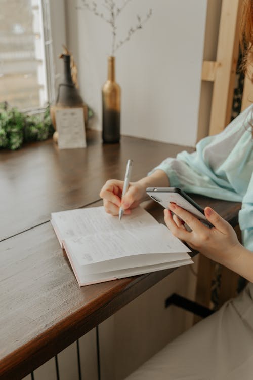 Free Crop woman with smartphone writing in notebook at home Stock Photo