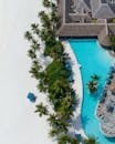 Aerial drone shot of exotic resort with empty hotel territory with green palms and blue swimming pool with sunbeds in sunlight