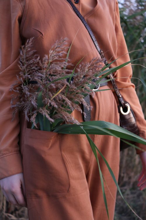 Free Unrecognizable crop female in orange outfit standing in field with blooming wildflowers in pocket Stock Photo