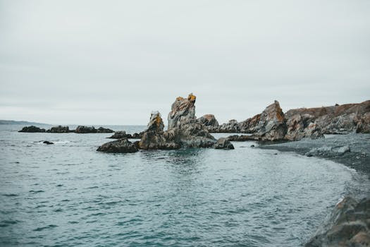 Tranquil view of rocky coastal formations against a cloudy sky, showcasing serene ocean waters.