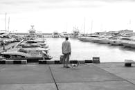 一张宁静的黑白图像中，一个男人和他的狗在港口俯瞰着游艇