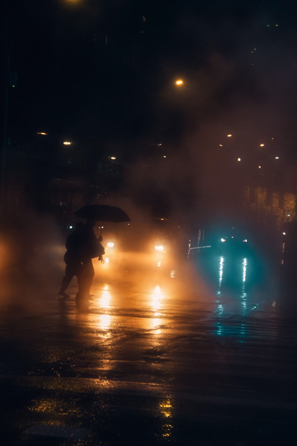 People with umbrellas walking on a wet road at night