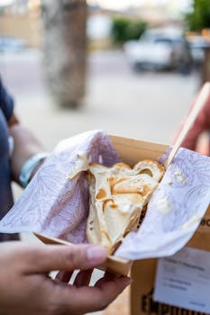Close-up of a person holding a crepe with whipped cream outdoors.