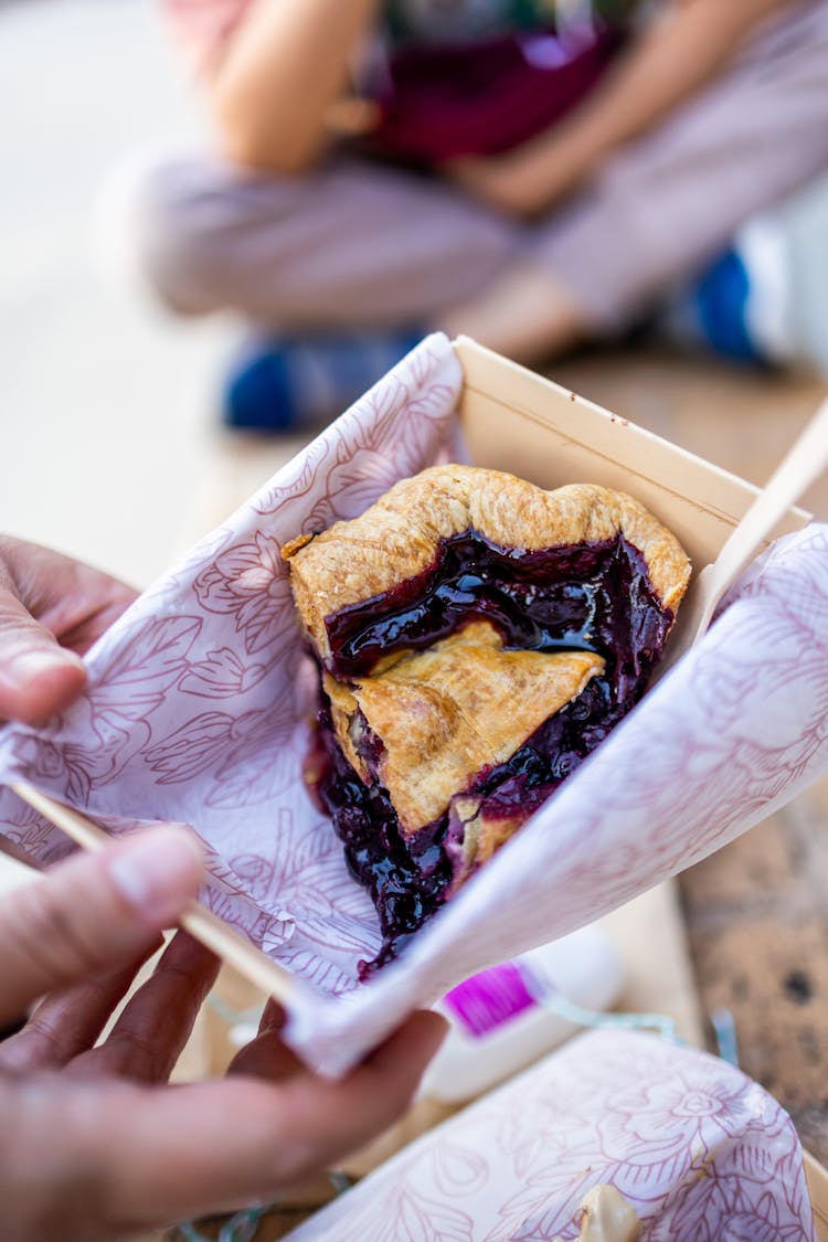 Person Holding A Slice Of Blueberry Pie In A Box