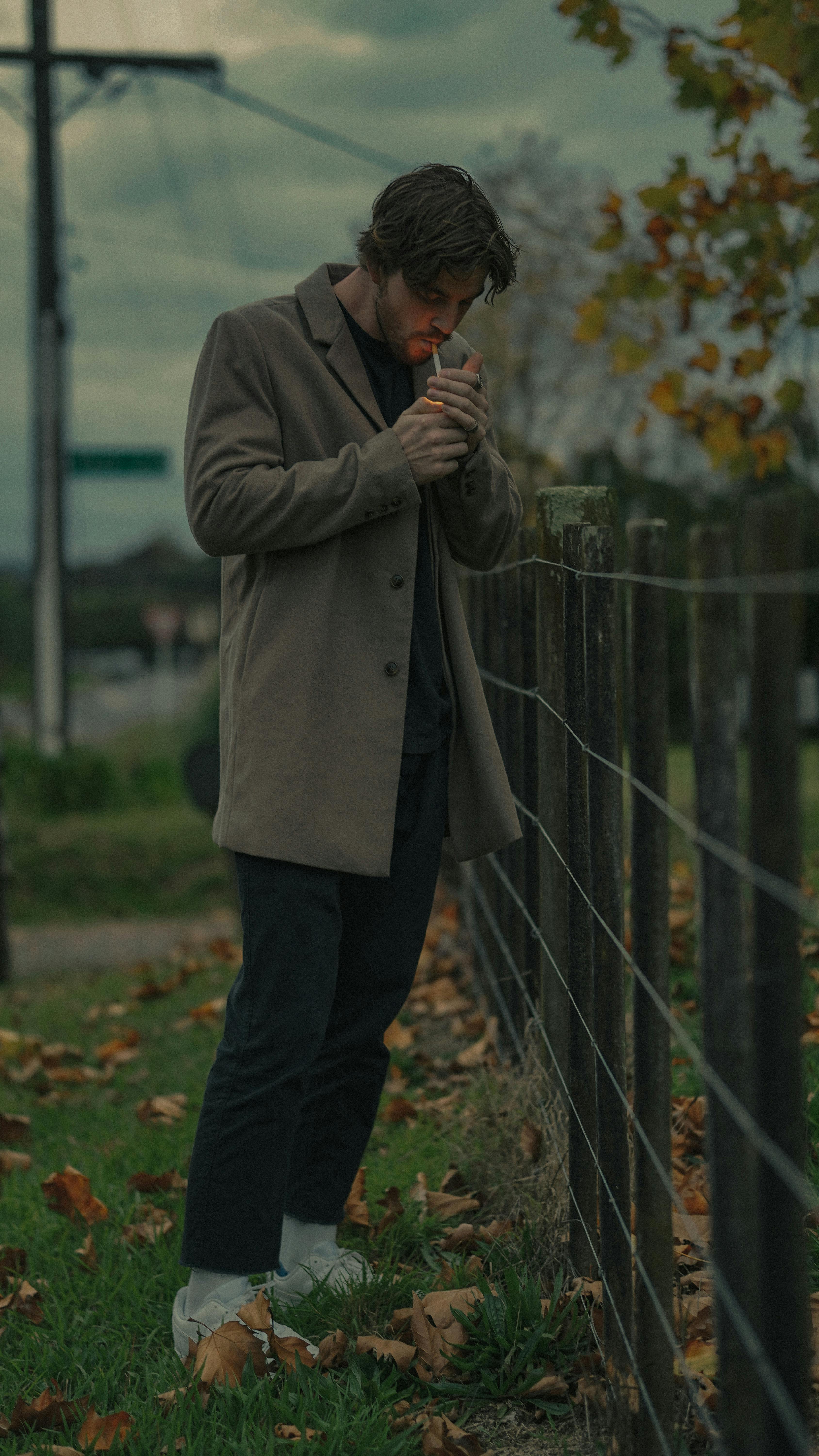 A Man Wearing a Brown Sweat Shirt Smoking on a Wooden Dock Near