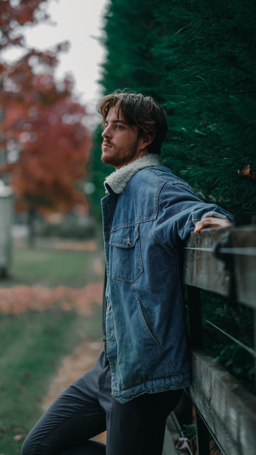 A Man in Denim Jacket Leaning on a Wooden Fence · Free Stock Photo