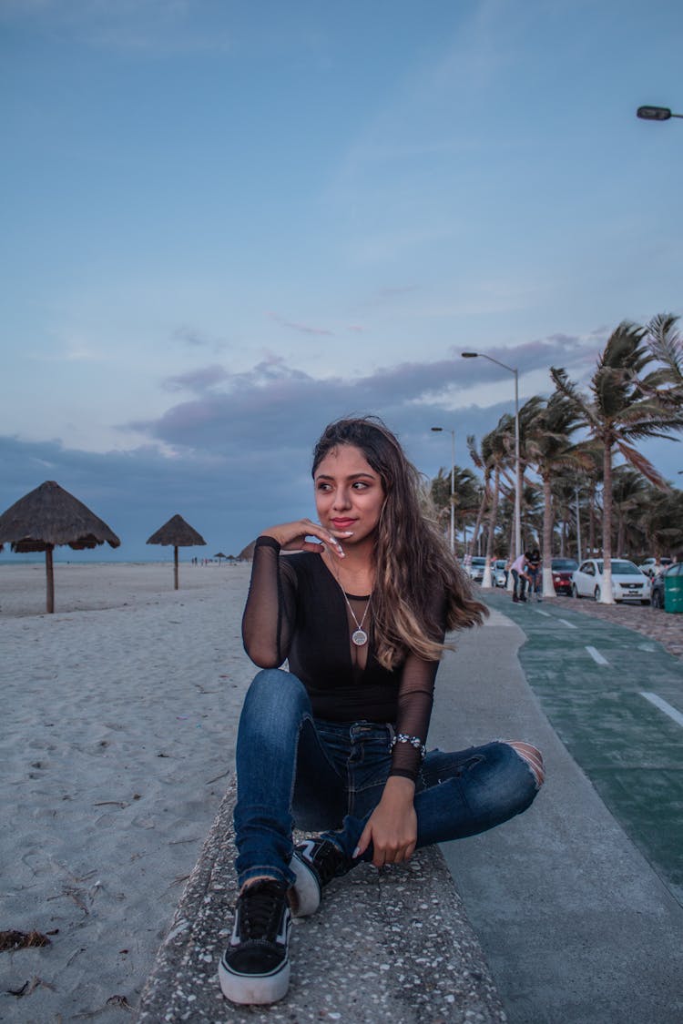 A Pretty Woman In Black Top Sitting On A Concrete Bench While Posing