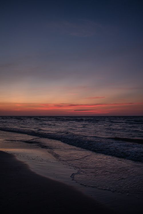 Free A serene beach scene at sunset with a tranquil ocean reflecting the vibrant sky colors. Stock Photo