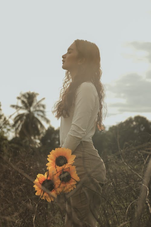 Side View of a Young Woman Holding Sunflowers
