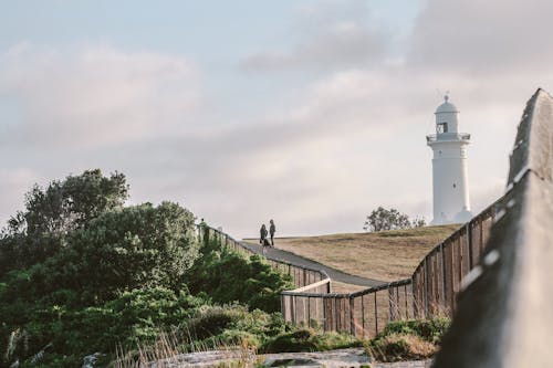Two Person Standing Near White Lighthouse