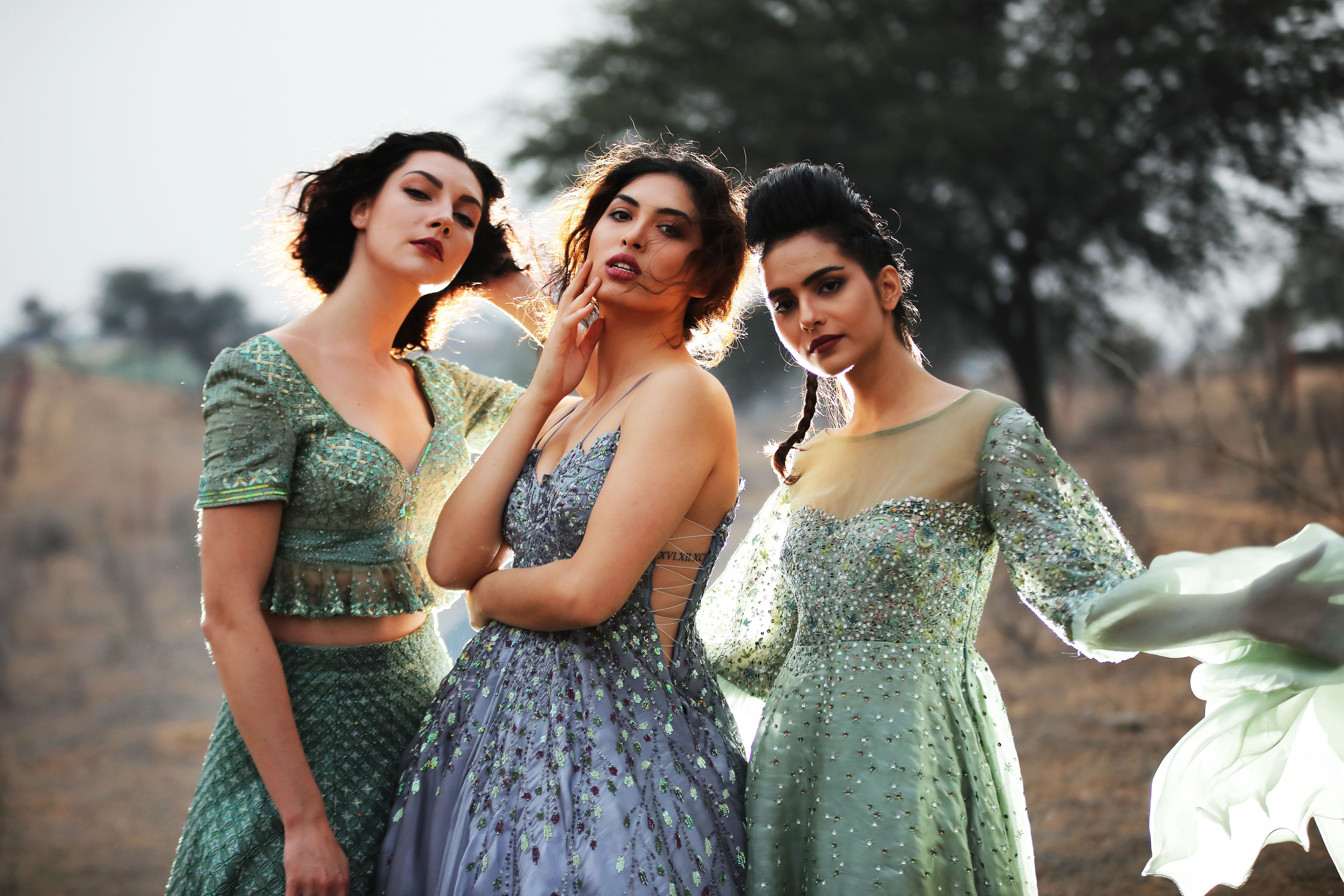 Three women posing elegantly in stylish dresses in an outdoor setting.
