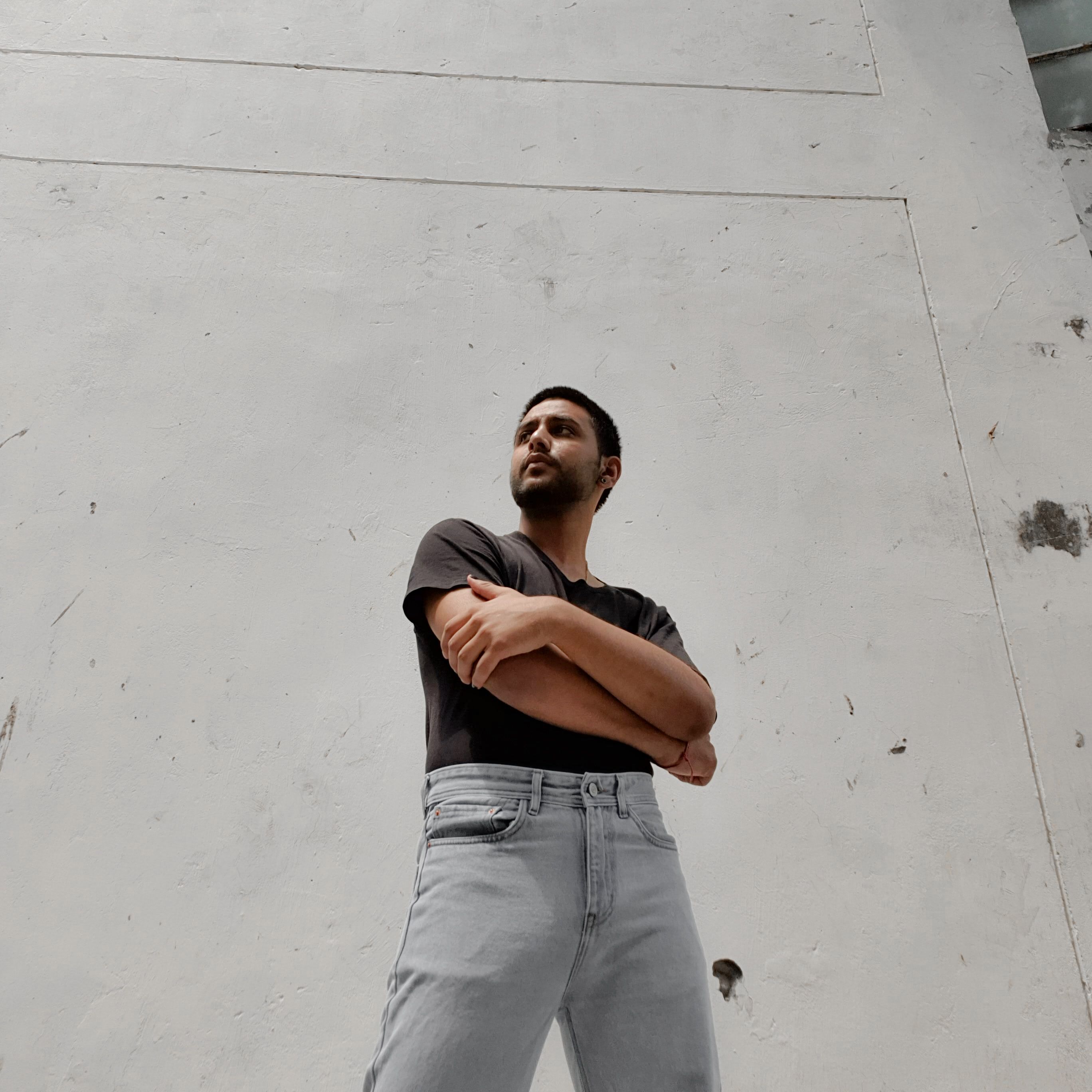Man in a plain dark crew-neck top standing against a pale concrete wall — photo by Animesh Srivastava on Pexels