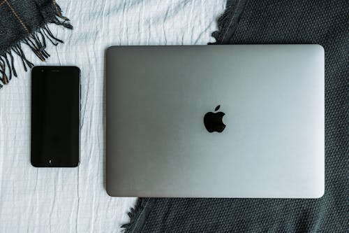 Overhead Shot of a Silver Laptop Beside a Black Cell Phone