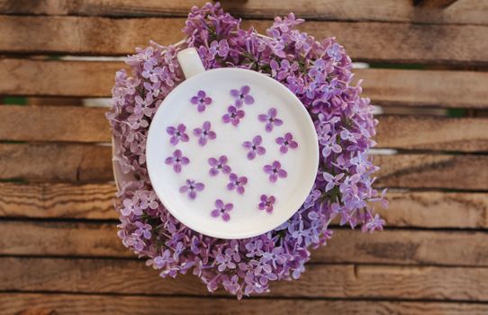 Top view of a tea cup with floating lilac flowers on a rustic wooden table, perfect for spring themes.