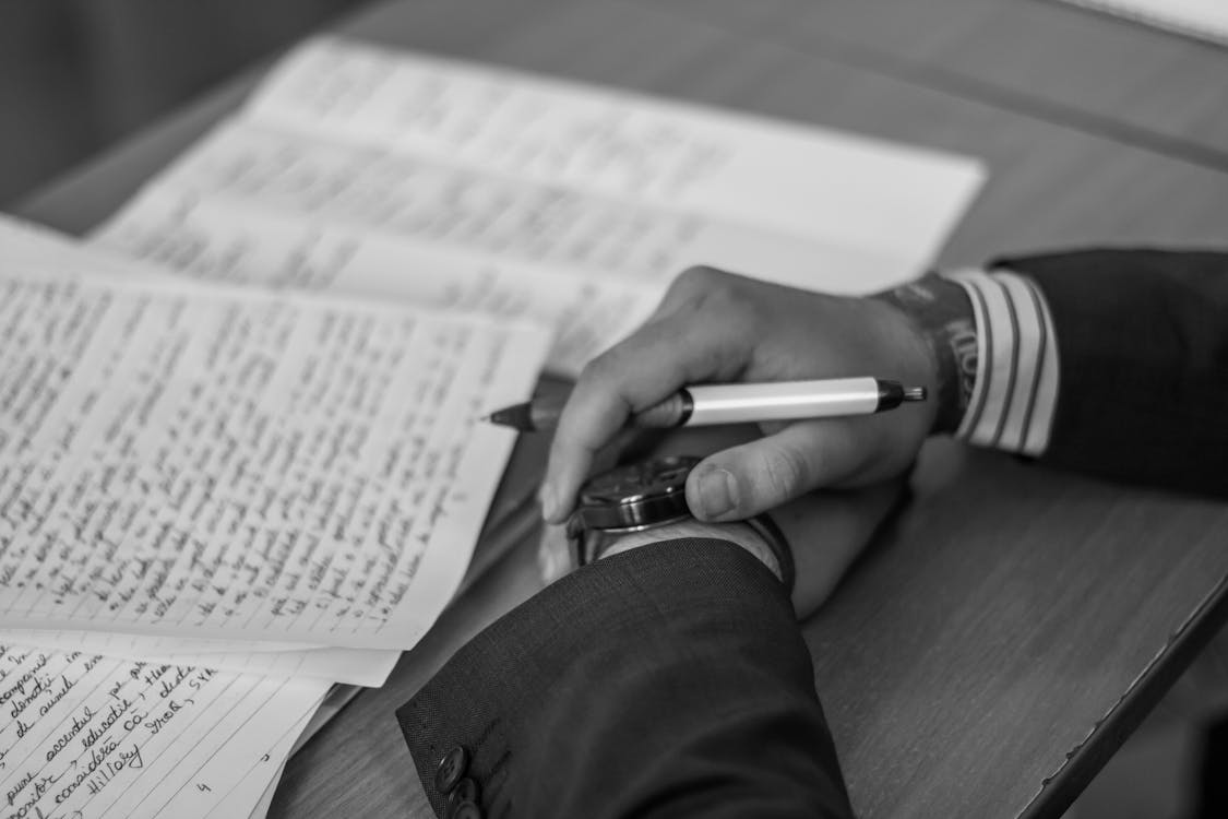Black and white photo of hands in front of a notebook. The person is wearing a suit and a nice watch.