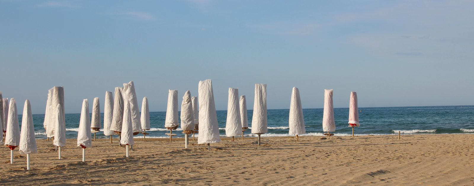 A serene beach scene with closed umbrellas and gentle waves in Abruzzo, Italy.