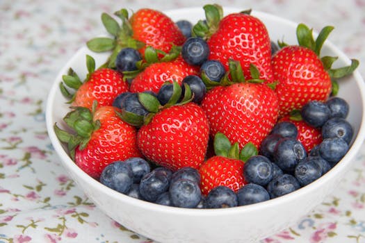 A vibrant mix of ripe strawberries and blueberries in a white bowl on a floral tablecloth.