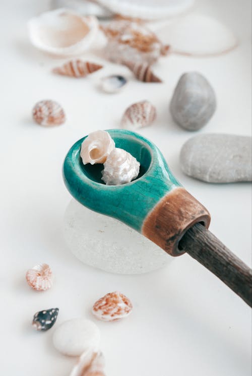 From above of wooden spoon putting small light seashells on white table in daytime