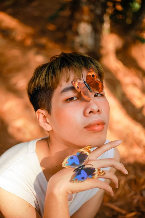 Free A captivating portrait of a young man with butterflies resting on his face and hand. Stock Photo