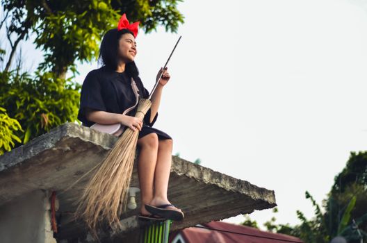 Smiling young woman with a broomstick sitting on a rooftop in Majayjay, Philippines.