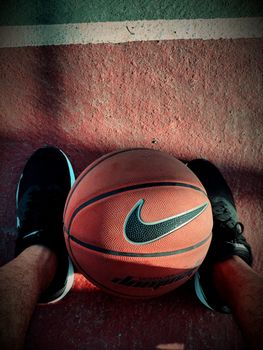 Basketball positioned on an outdoor court, framed by black sneakers, emphasizing sports and footwear.