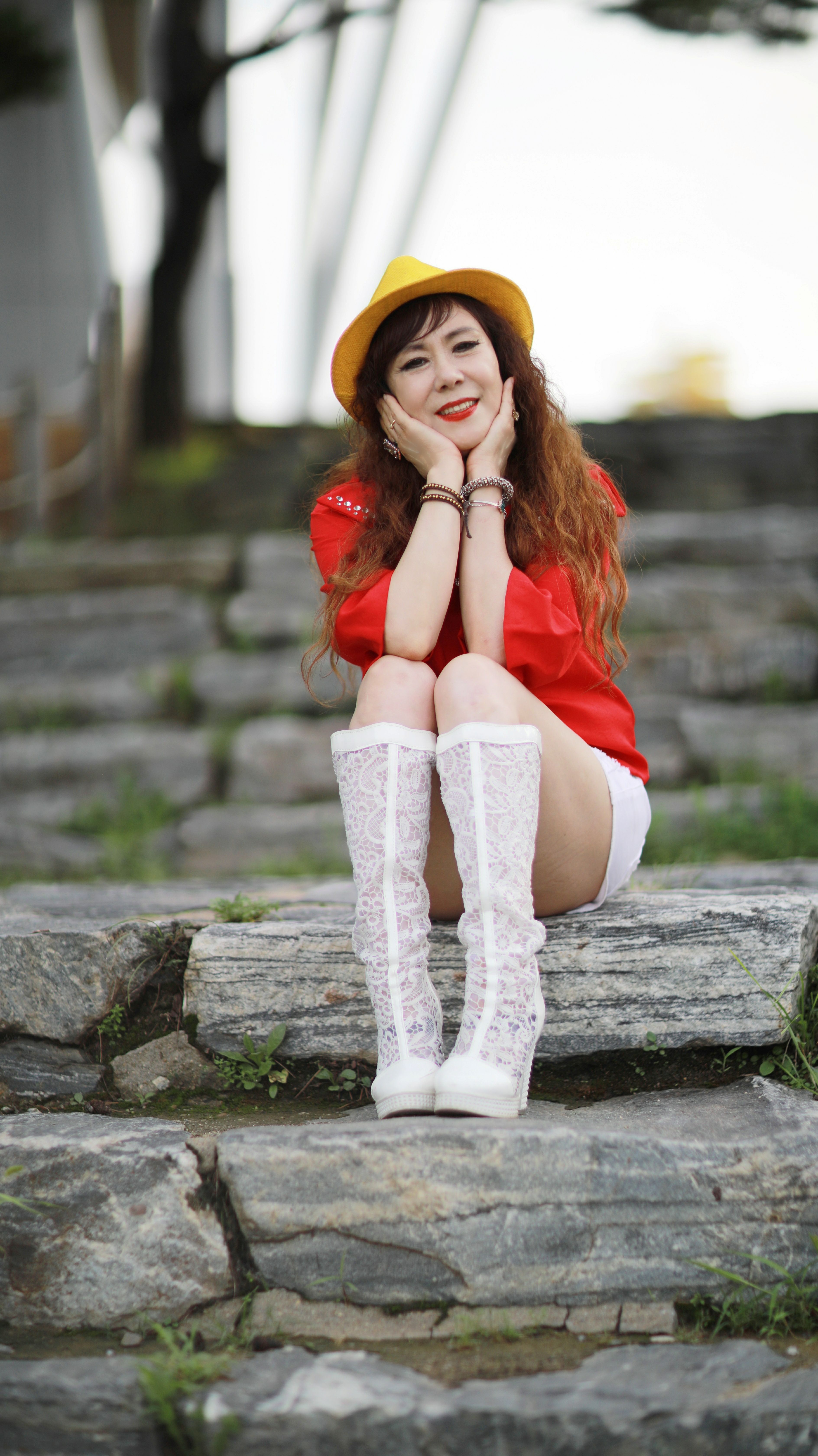 Happy woman in a fedora and boots sitting on stone steps outdoors.