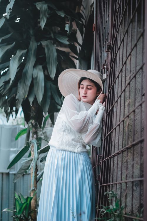Free Elegant woman in stylish outfit and wide-brimmed hat poses gracefully against a fence, outdoors. Stock Photo