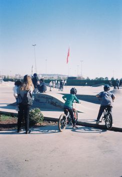 Kids riding bicycles at an outdoor skate park on a sunny day.