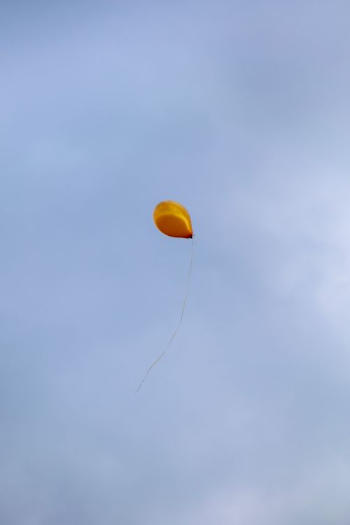 Free A single yellow balloon drifting against a gray sky, symbolizing freedom. Stock Photo