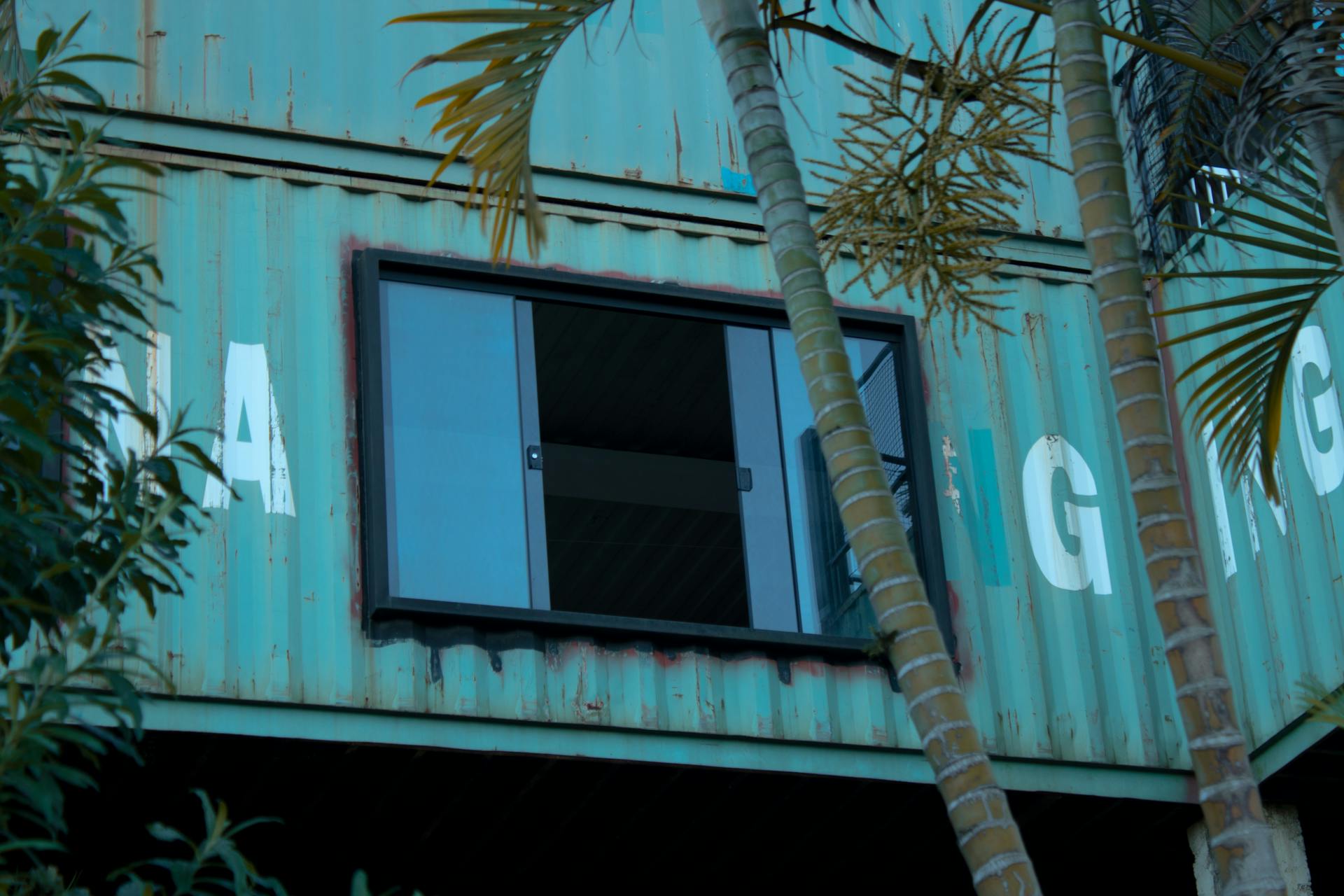 Unique architectural facade using shipping containers with palm trees in the foreground.