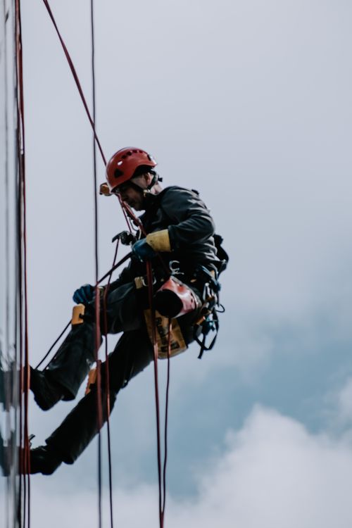 Free Professional worker rappelling down a building facade for maintenance. Stock Photo