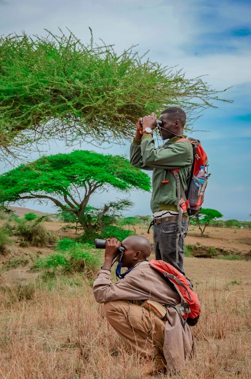 Men Looking Through the Binoculars While Standing on the Grassland