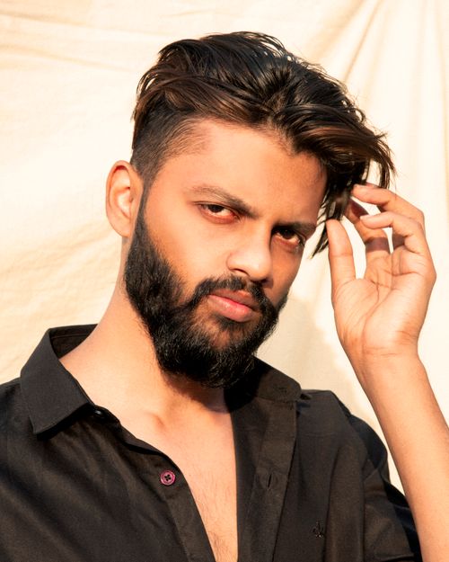 Free Close-up portrait of a bearded man in a black shirt adjusting his hair against a simple background. Stock Photo