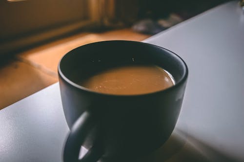 テーブルの上の茶色のコーヒーで満たされた黒いセラミックマグの浅い焦点の写真