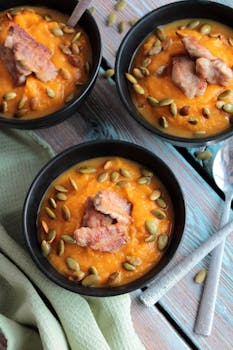 Three bowls of creamy pumpkin soup garnished with roasted chicken and seeds for a hearty meal.