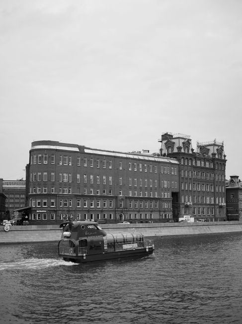 A vintage-style black and white photograph featuring a boat on the Moscow River against historic architecture.