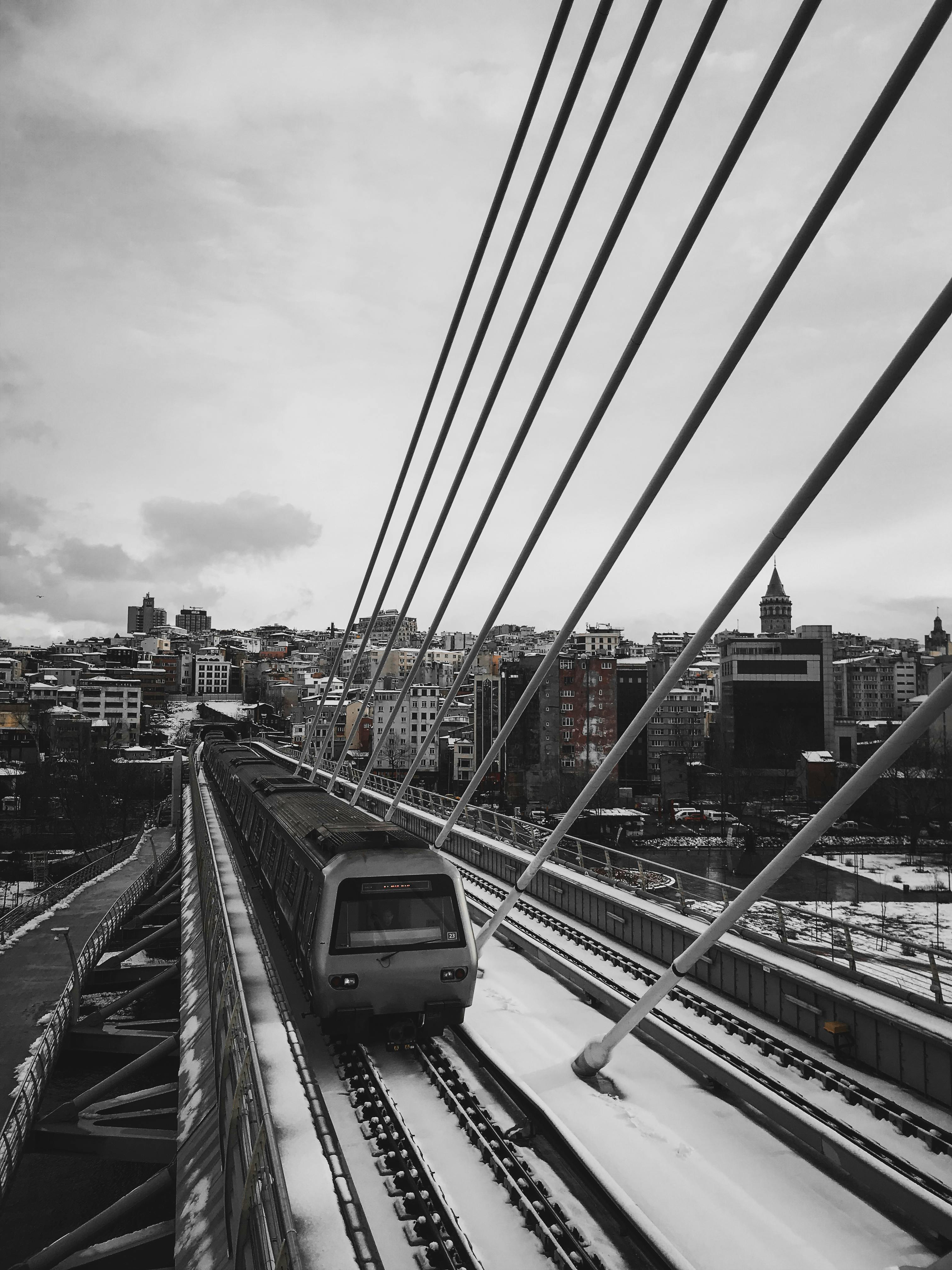 Free A train crosses a snowy bridge in a bustling city, showcasing modern transportation amid urban architecture. Stock Photo