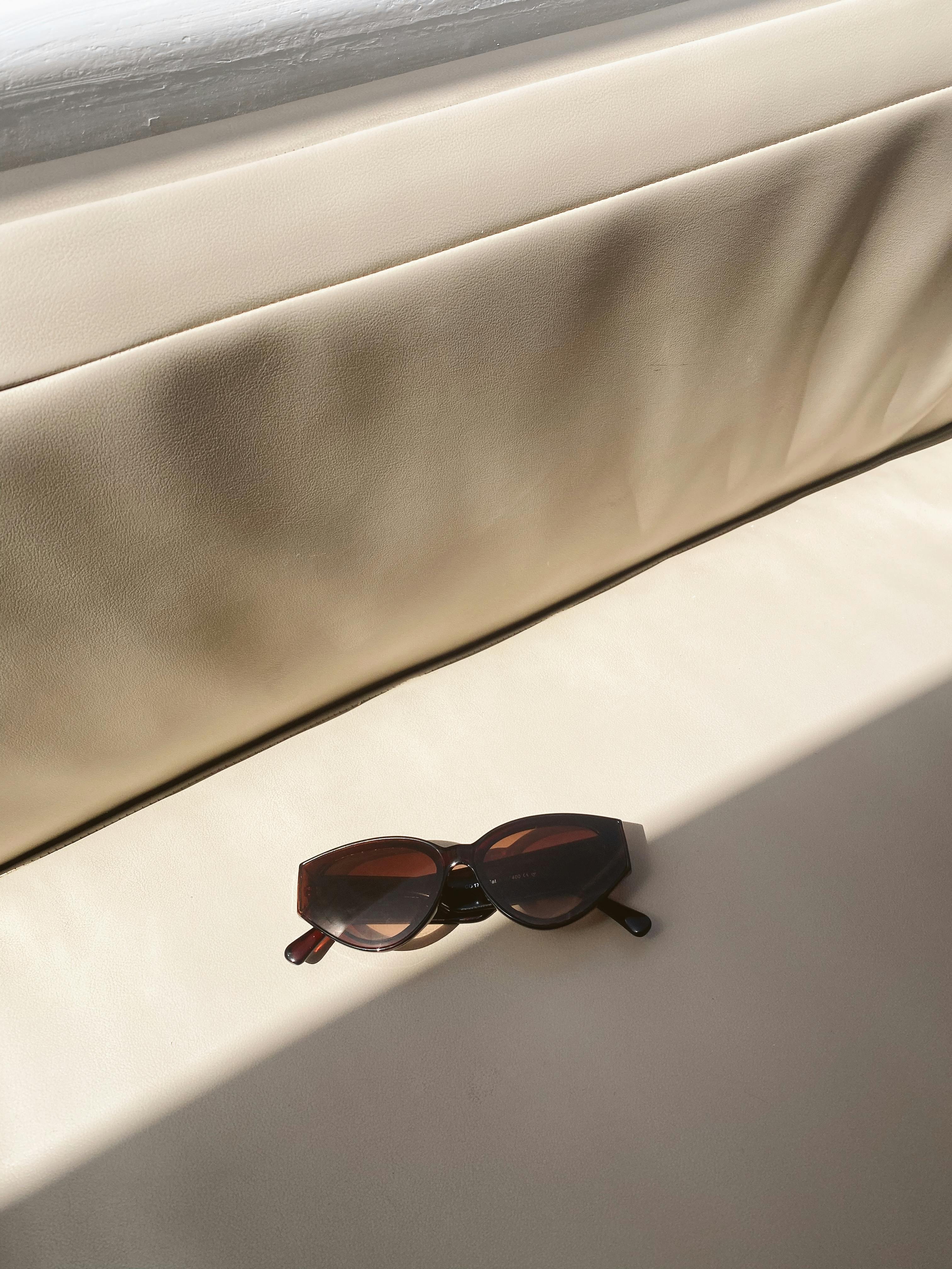 Cat-eye sunglasses resting on a sunlit cream sofa, casting soft shadows.