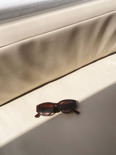 Cat-eye sunglasses resting on a sunlit cream sofa, casting soft shadows.
