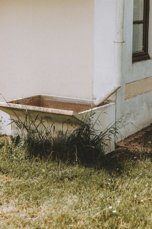 Free Exterior of shabby building with water tank placed under white pipe on grassy ground in summer Stock Photo
