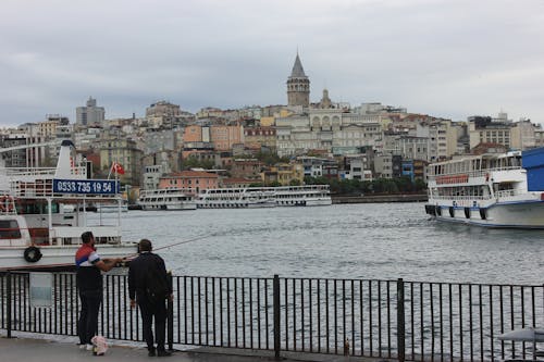 Free Man Fishing on a Bridge and the Cityscape of Istanbul on a Cloudy Day  Stock Photo