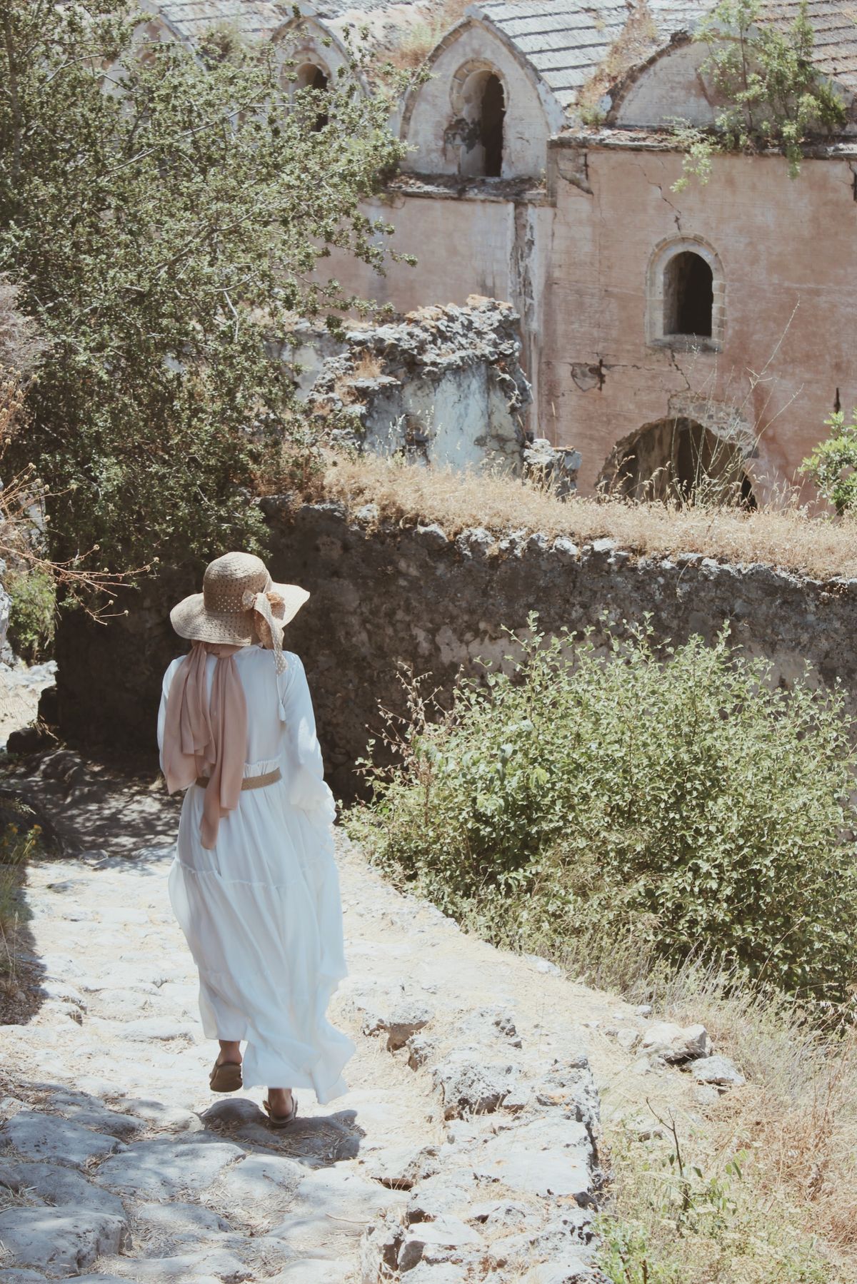 A woman in a white dress walking on a pathway — linen ease in the European summer light