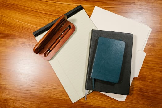 An overhead view of office supplies including a pen, notebook, and folder on a wooden desk.